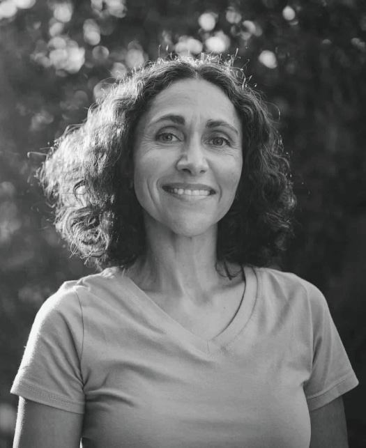 Black-and-white portrait of a smiling woman with curly hair outdoors.